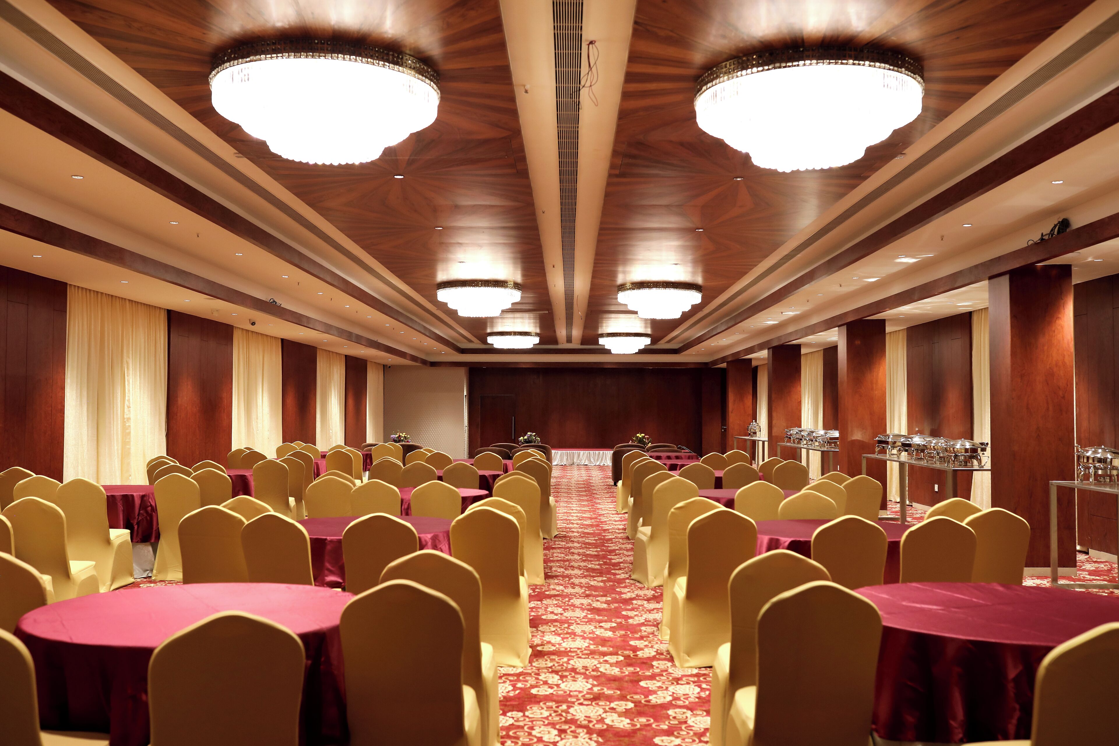 Un salón de conferencias con filas de mesas y sillas, candelabros y alfombra roja.