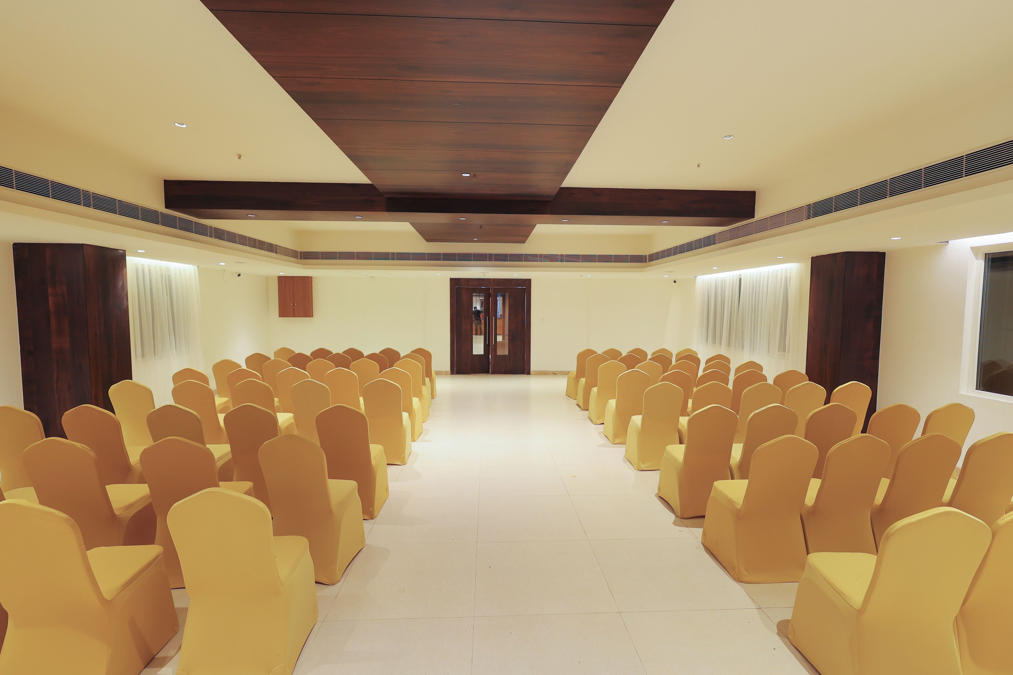 A conference room with rows of yellow chairs, a wooden ceiling, and a tiled floor.