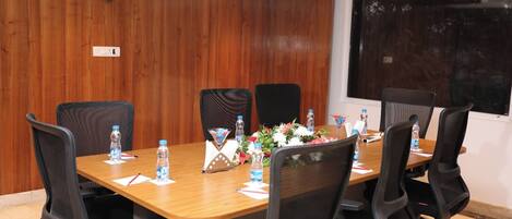 A conference room with a wooden paneled wall, a large table with chairs, water bottles, a flower arrangement, and a projector screen.