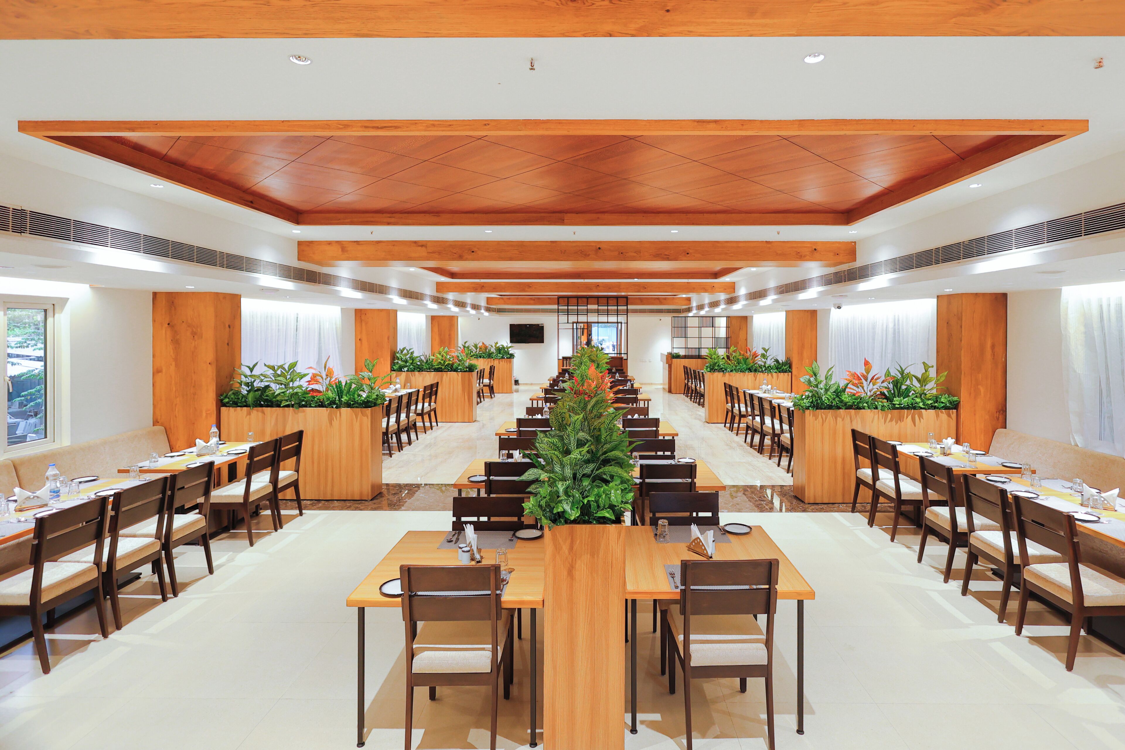 A spacious dining area with long wooden tables and chairs, centered around a large plant.
