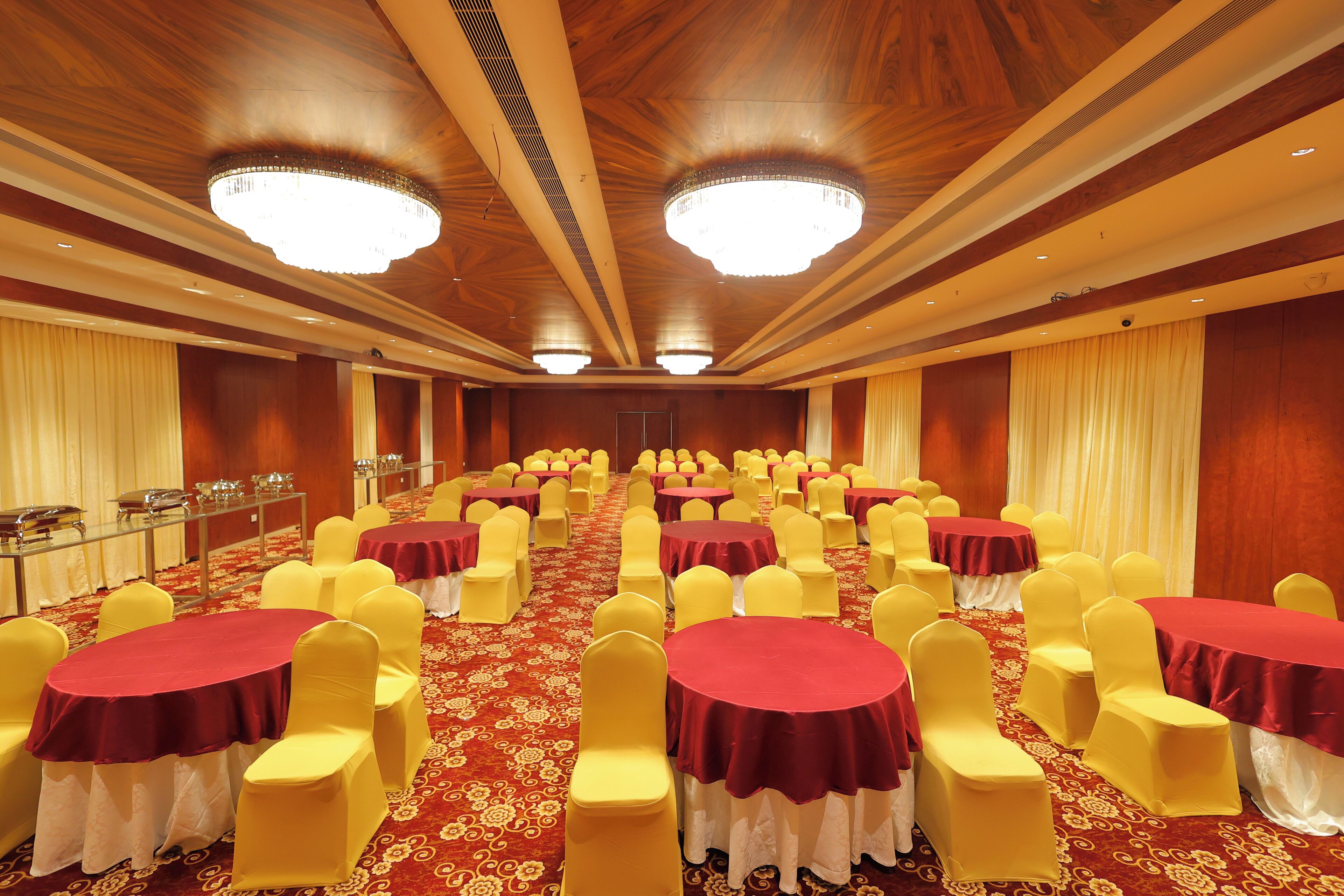 A large conference room with rows of tables and chairs, wooden paneling, and chandeliers.