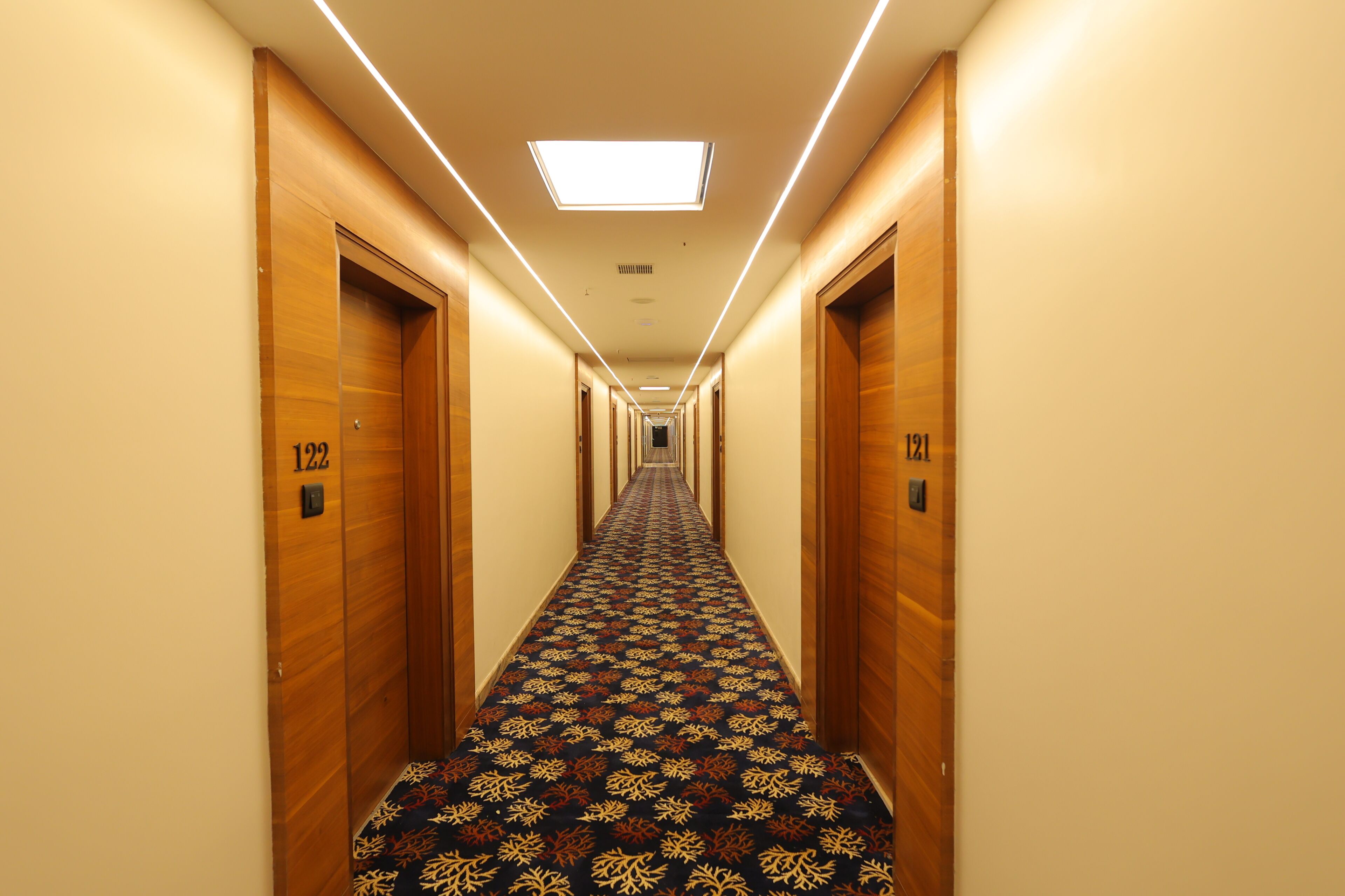 A hotel hallway with wooden doors numbered 122 and 191, carpeted with a patterned design, and a ceiling light.