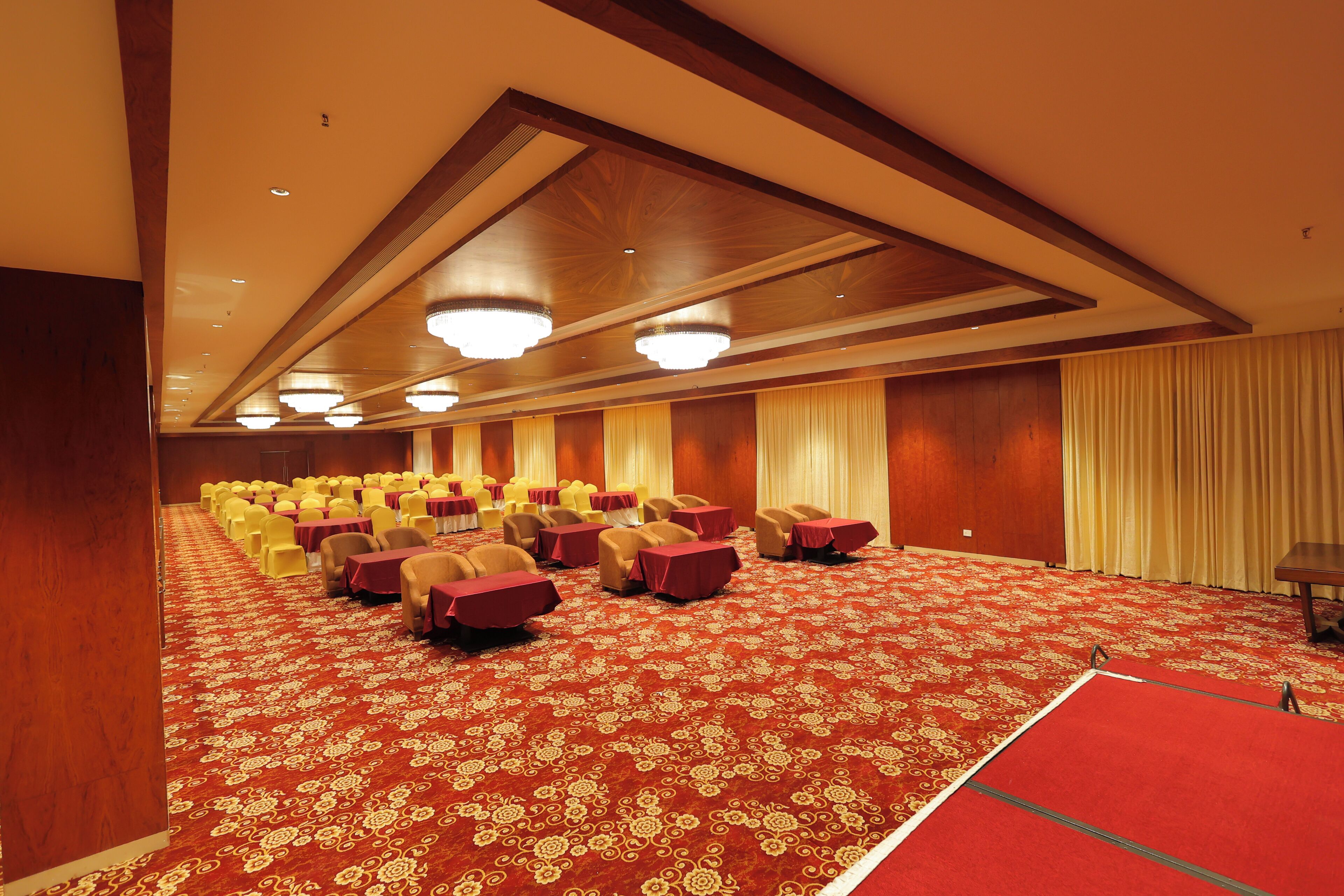 Un salón de conferencias con filas de mesas y sillas, una alfombra estampada y paneles de madera en las paredes.