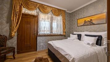 Un dormitorio con puerta de madera, una cama grande con ropa de cama blanca, una silla y un cuadro con atardecer sobre agua.