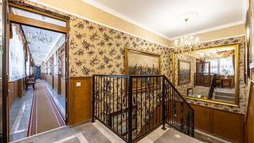 A grand staircase with ornate black railings, a patterned wallpaper, and a chandelier.
