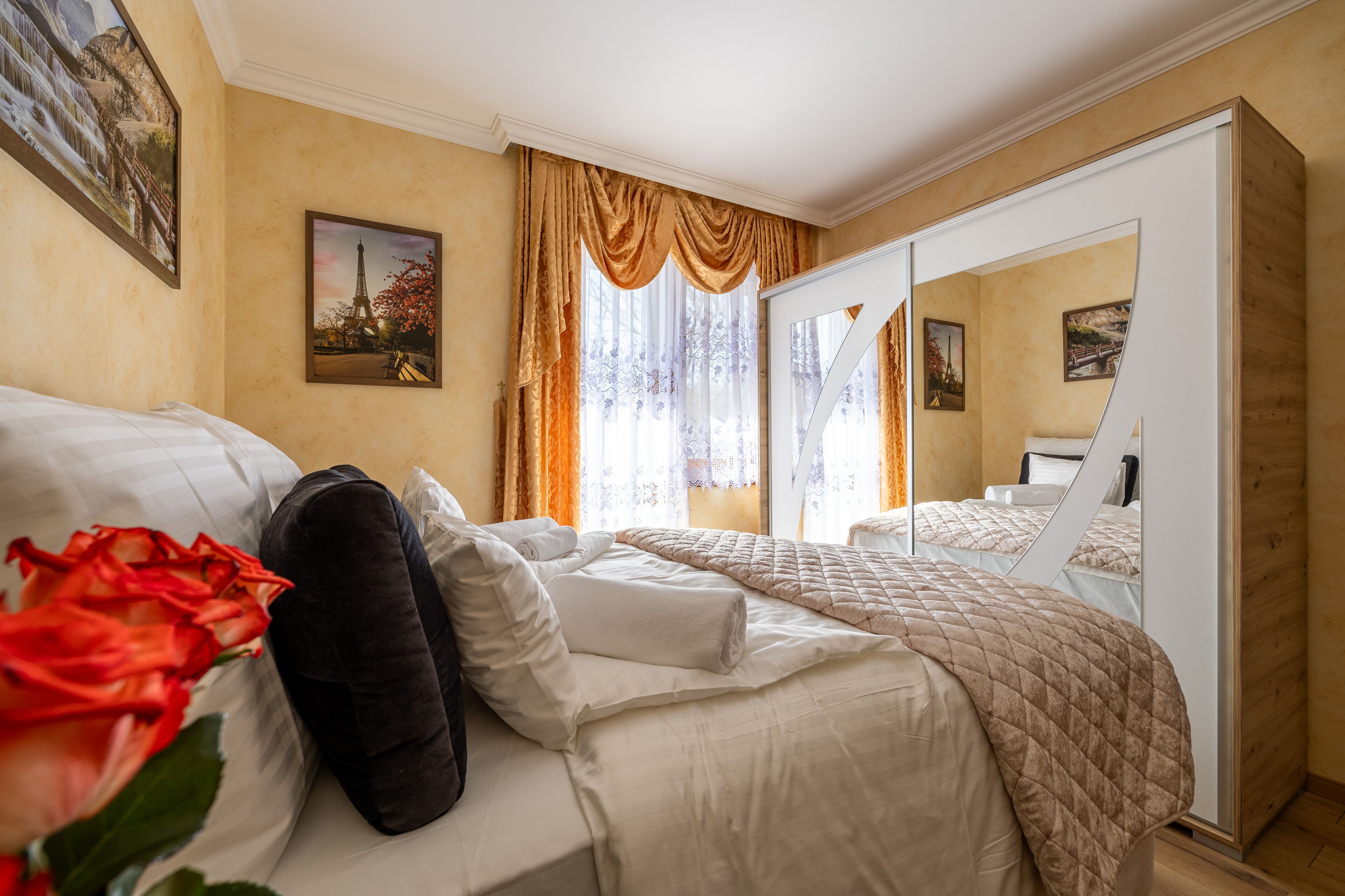A hotel room with a bed, a mirror, and a window with curtains.
