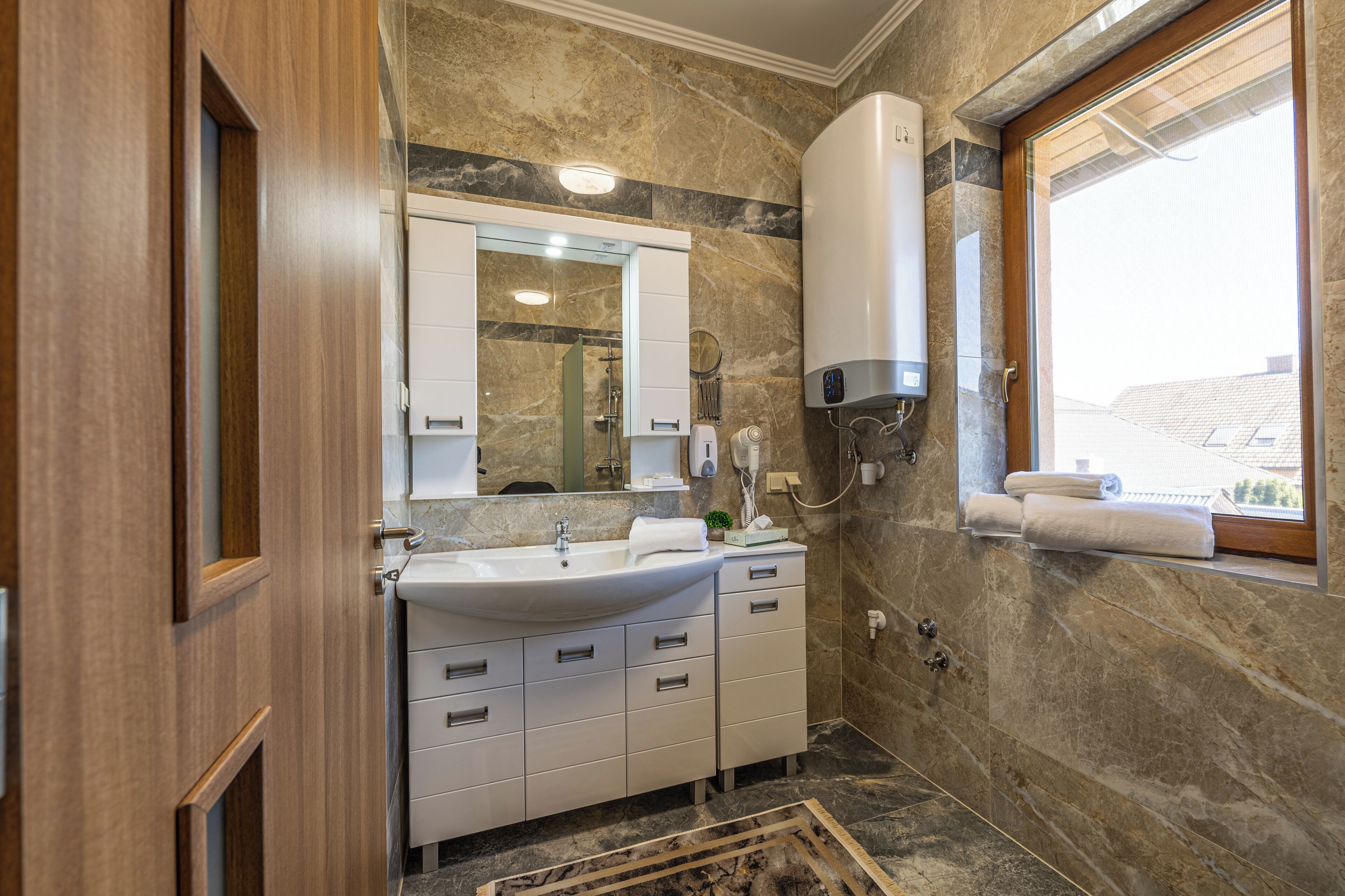 A bathroom with a marble wall, a sink, a mirror, a towel rack, and a window with a view.
