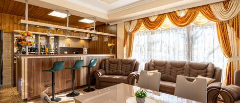 A modern living room with a glass coffee table, leather sofas, and a bar area with stools.