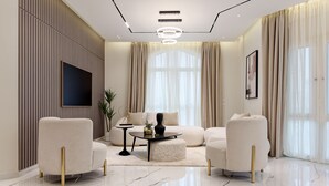 A modern living room with a sofa, two armchairs, a coffee table, and a TV mounted on the wall. - VESTA - Heliopolis Residence (Cairo)