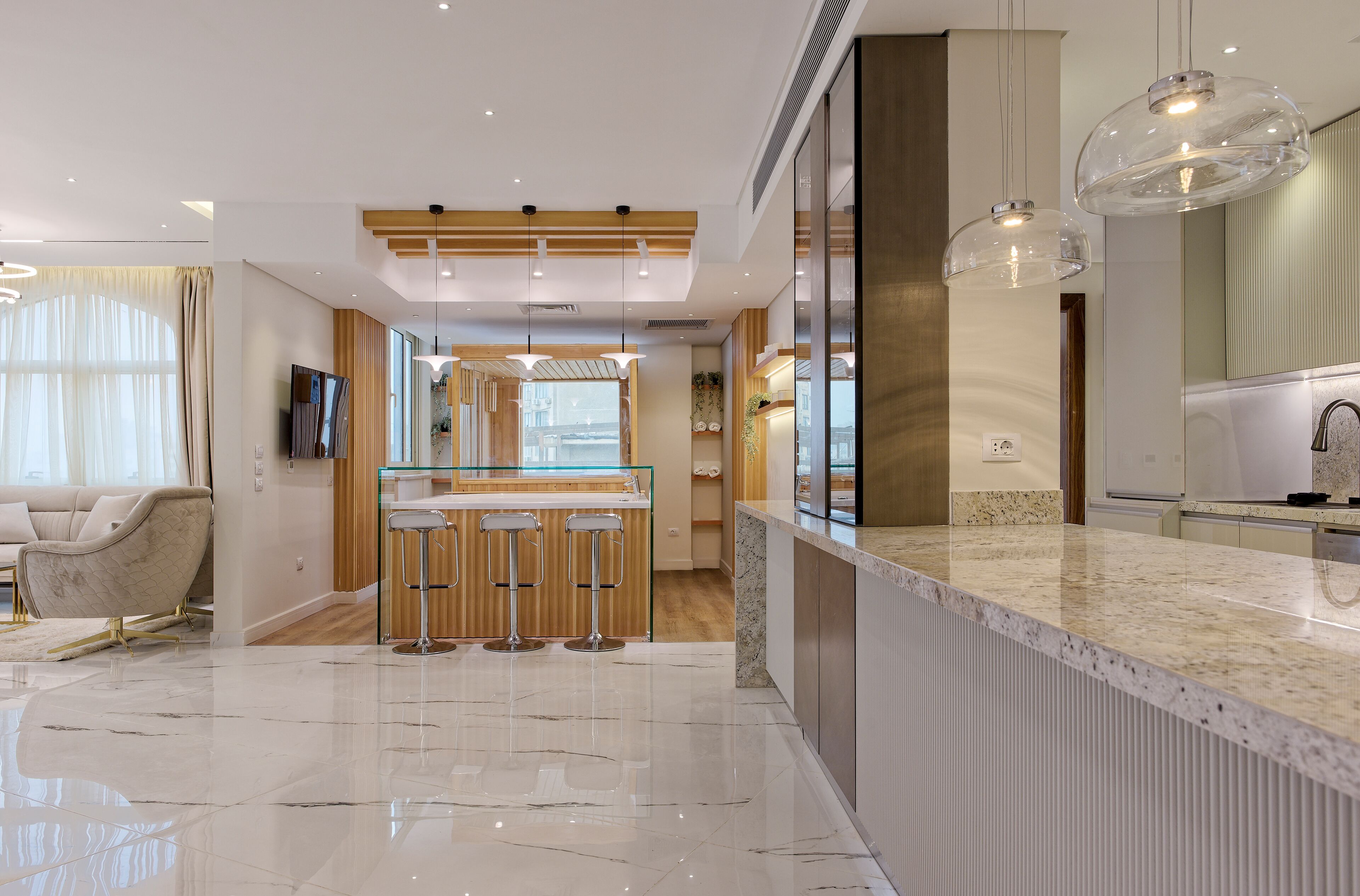 A modern kitchen with a marble countertop, wooden bar stools, and pendant lighting.
