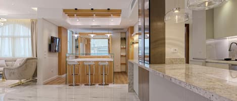 A modern kitchen with a marble countertop, wooden bar stools, and pendant lighting.