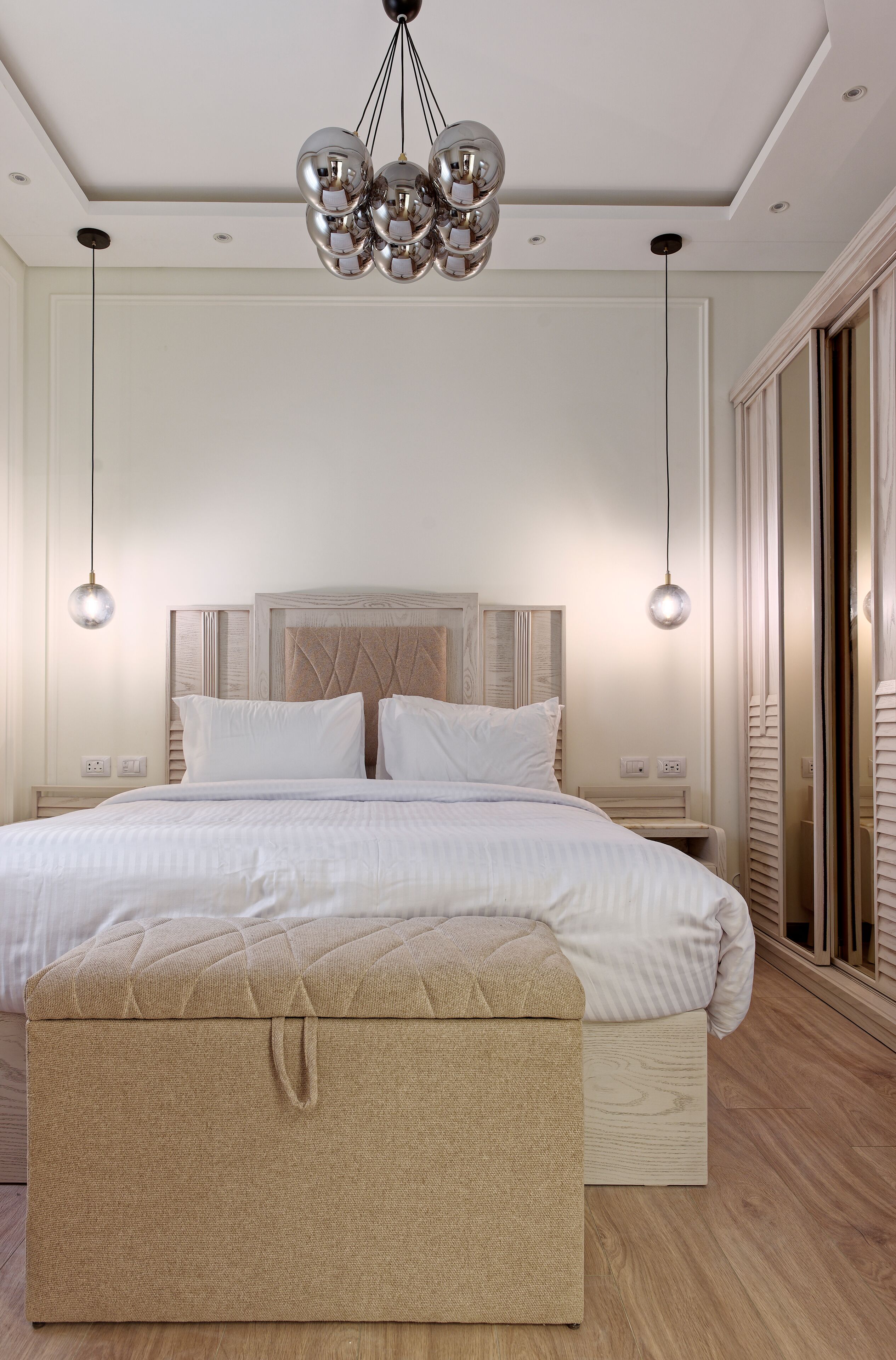 A modern bedroom with a large bed, a chest of drawers, a hanging light fixture, and a sliding glass door.
