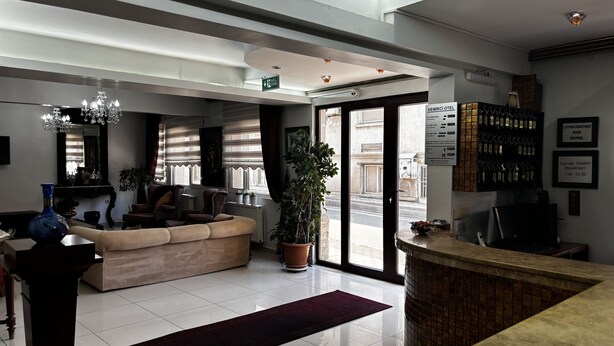 A modern hotel lobby with a reception desk, seating area, and a large window offering a view of the street. - Demirci Otel (Bursa)