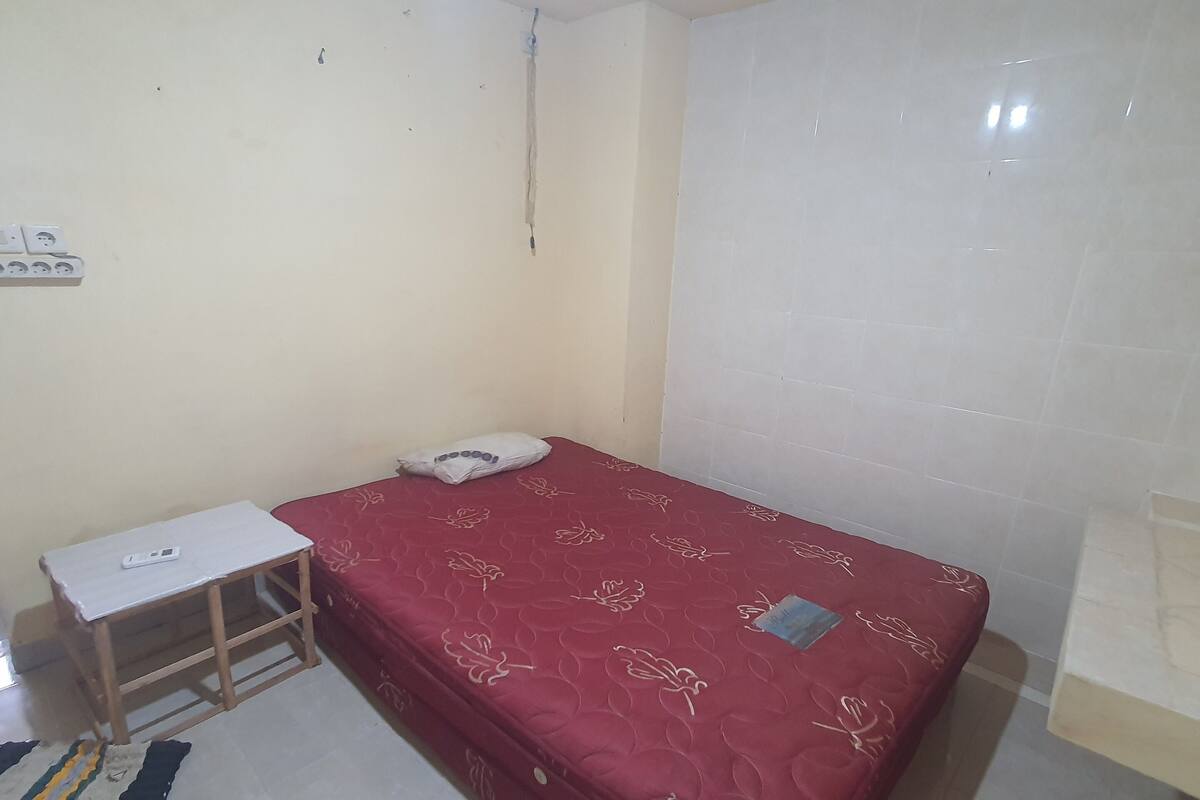 A small, simple room with a single bed, a small table, and a power outlet on the wall.
