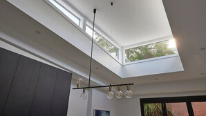 Ein modernes Interieur mit Dachfenster, Pendelleuchten und Blick auf Grün.