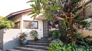 Una casa con una escalera que lleva a una puerta, rodeada de abundante follaje y plantas en macetas.
