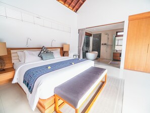 Un dormitorio moderno con una cama grande, mesitas de noche, un banco, un baño con bañera y ducha.