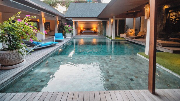 Una piscina con cubierta de madera, sillas de descanso y plantas en macetas.