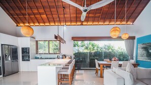 Una cocina moderna con una isla central, un comedor con un sofá y sillas blancos, y un ventilador de techo.