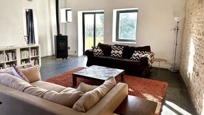 A modern living room with a sofa, coffee table, bookshelf, fireplace, and large windows. - Stylish Country House an hour from Paris (Chevrainvilliers)