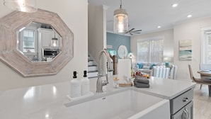 A modern kitchen with a white countertop, stainless steel sink, and a large mirror.
