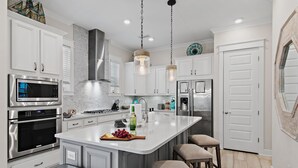 A modern kitchen with stainless steel appliances, a central island with bar stools, and pendant lighting.