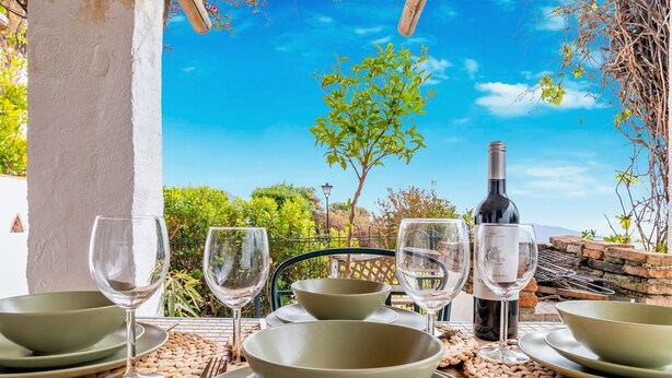 Une table dressée avec des bols, des verres à vin et une bouteille de vin, offrant une vue sur la verdure et un ciel dégagé.