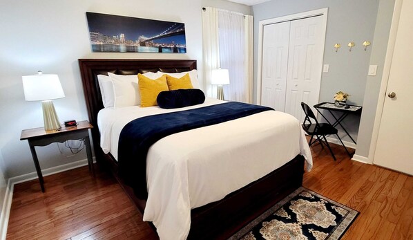 Una habitación de hotel ordenada con cama, lámparas de noche, una mesita con un florero y una puerta.
