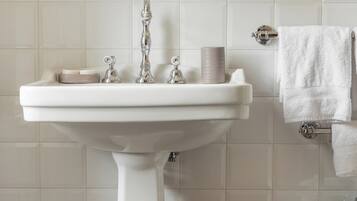 Un lavabo sur pied blanc, doté d’un robinet chromé, d’un porte-savon et d’une pile de serviettes blanches posées sur un mur carrelé.