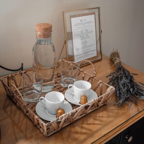 Una mesa con una botella corchada, dos tazas blancas con platillos, una taza de cobre pequeña y un menú enmarco.