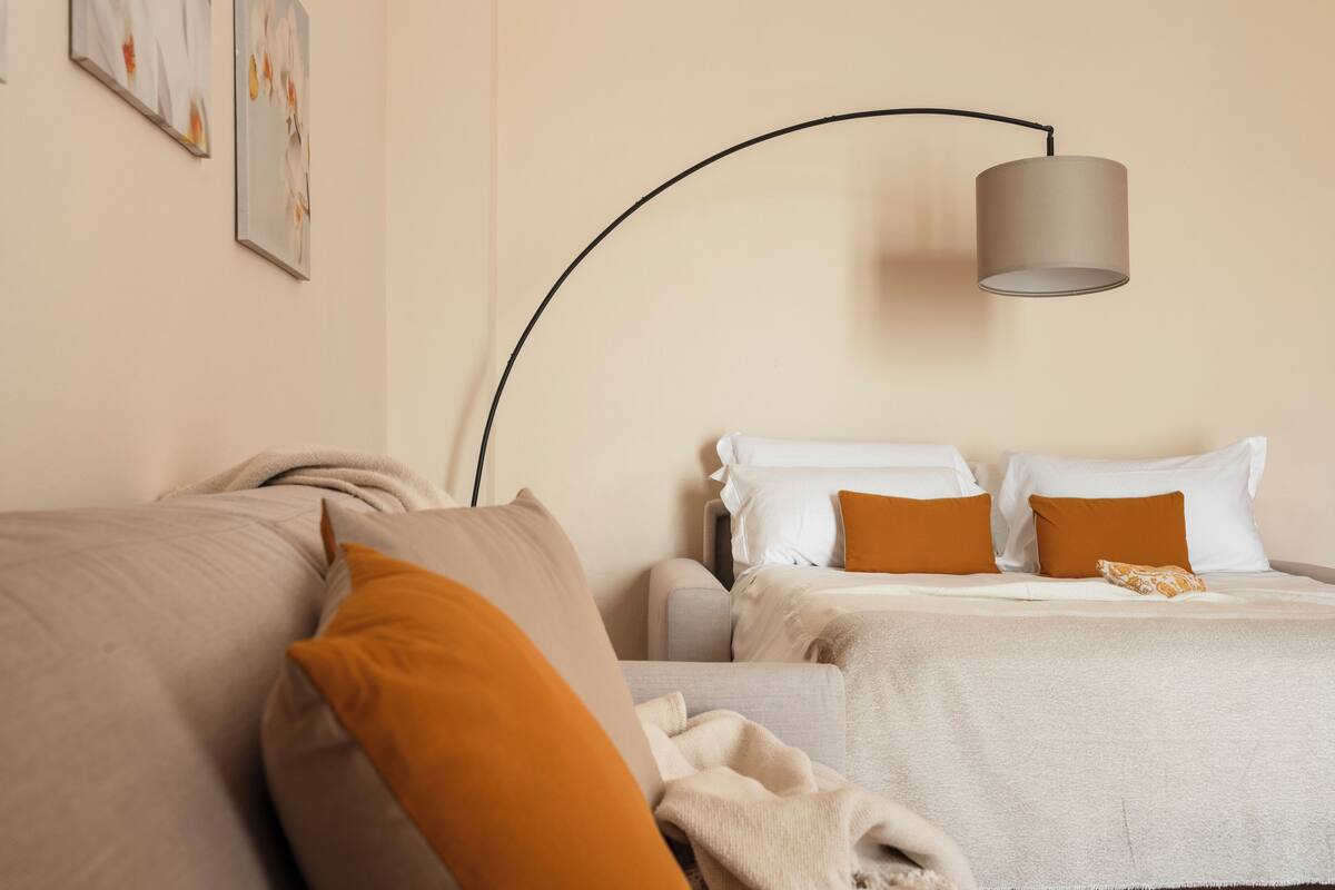Une chambre à coucher comprenant un lit, un canapé, une lampe sur pied et des œuvres d’art murales.