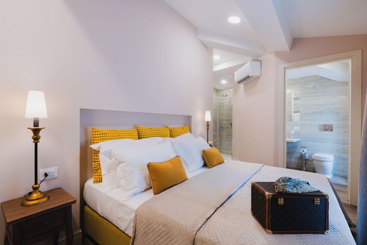 Une chambre d’hôtel avec un lit, une table de chevet, une lampe et une valise posée sur le sol.