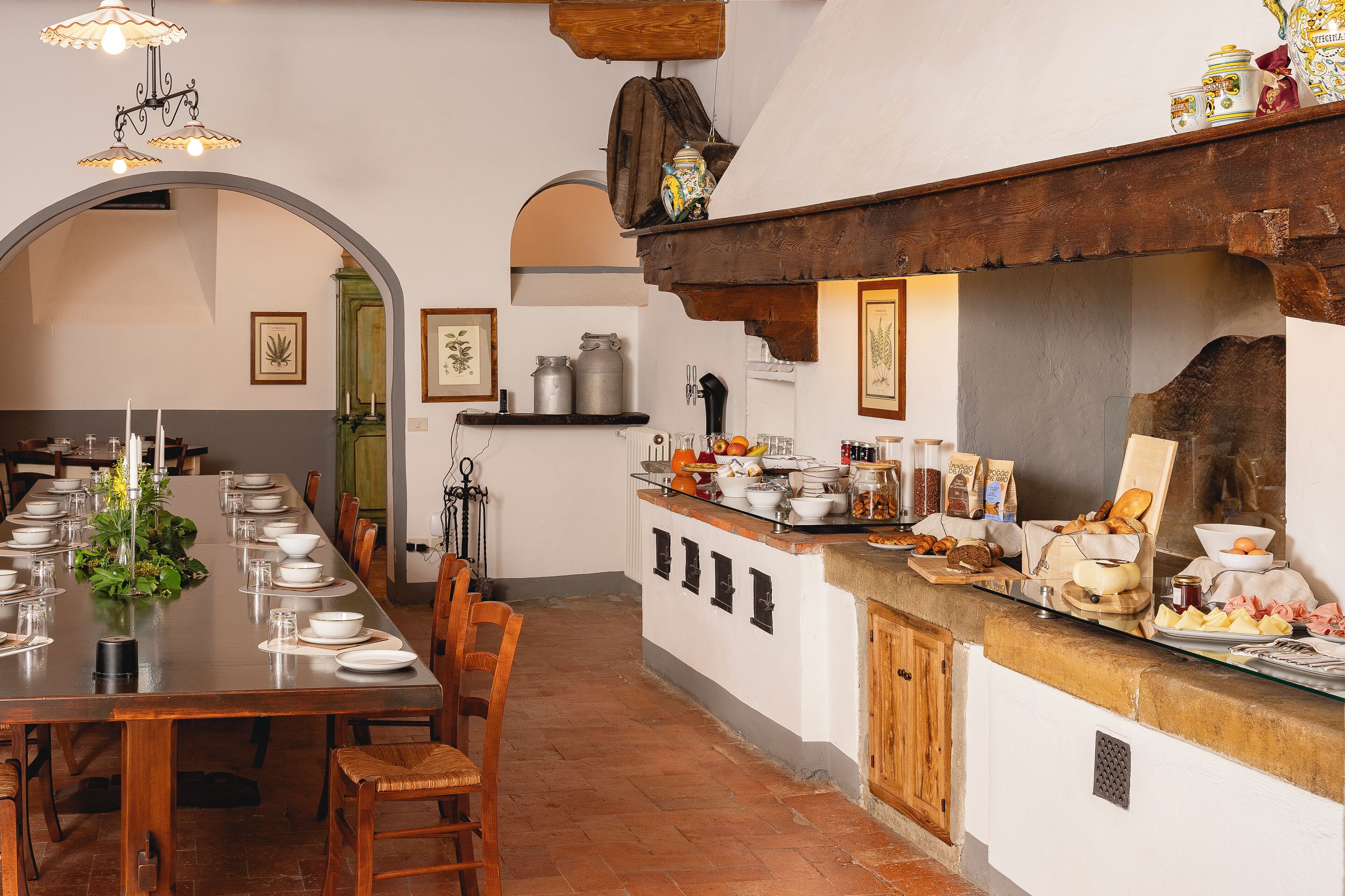 A dining area with a long table set for a meal, a kitchen counter with various food items, and a rustic wooden ceiling.