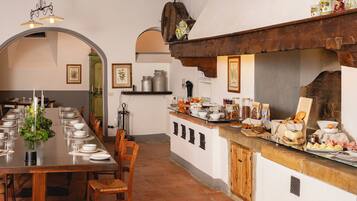 A dining area with a long table set for a meal, a kitchen counter with various food items, and a rustic wooden ceiling.