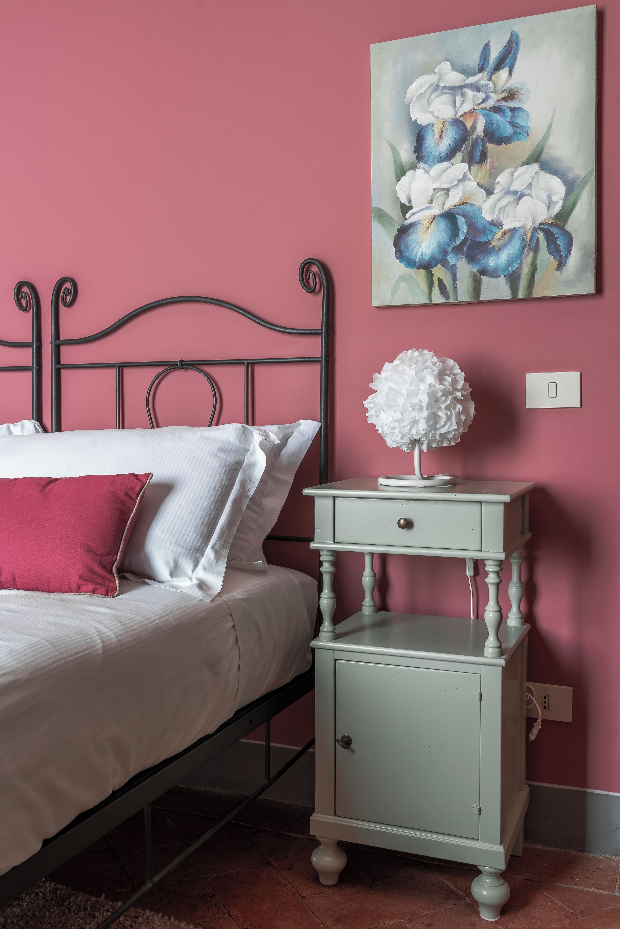A bedroom with a bed, a nightstand, a wall-mounted painting, and a power outlet.