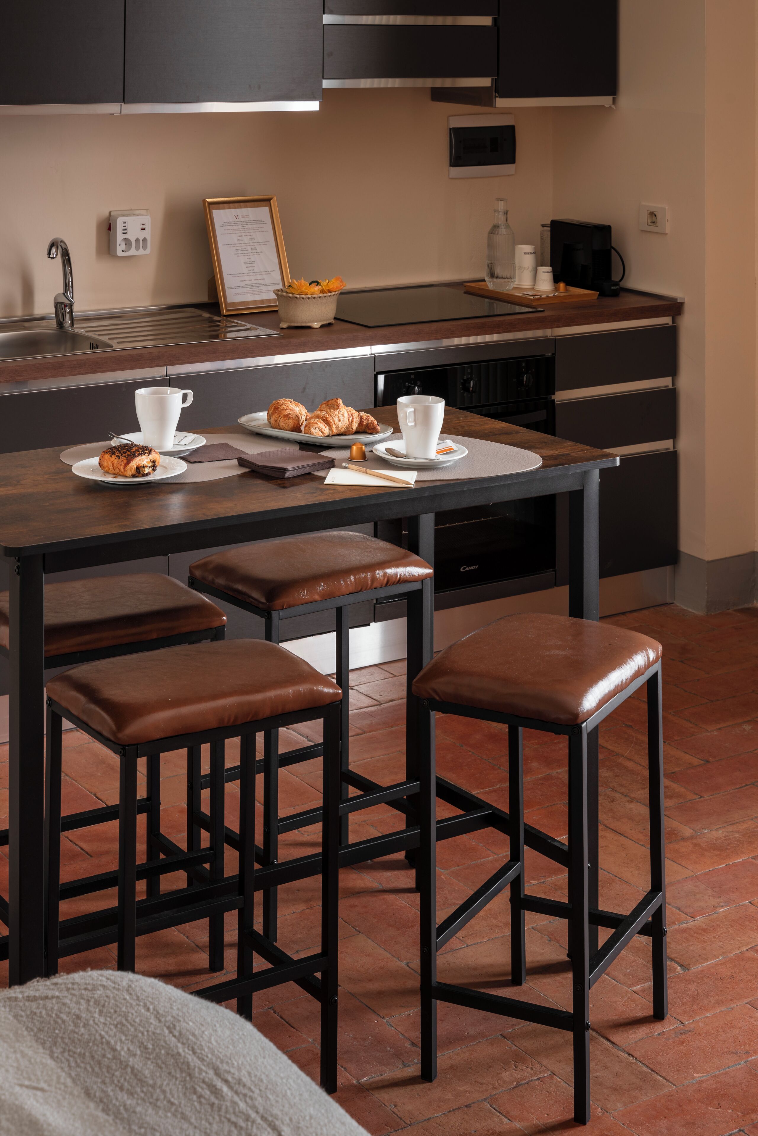 Cozinha moderna com ilha central, banquetas, máquina de café e cardápio emoldurado na parede.