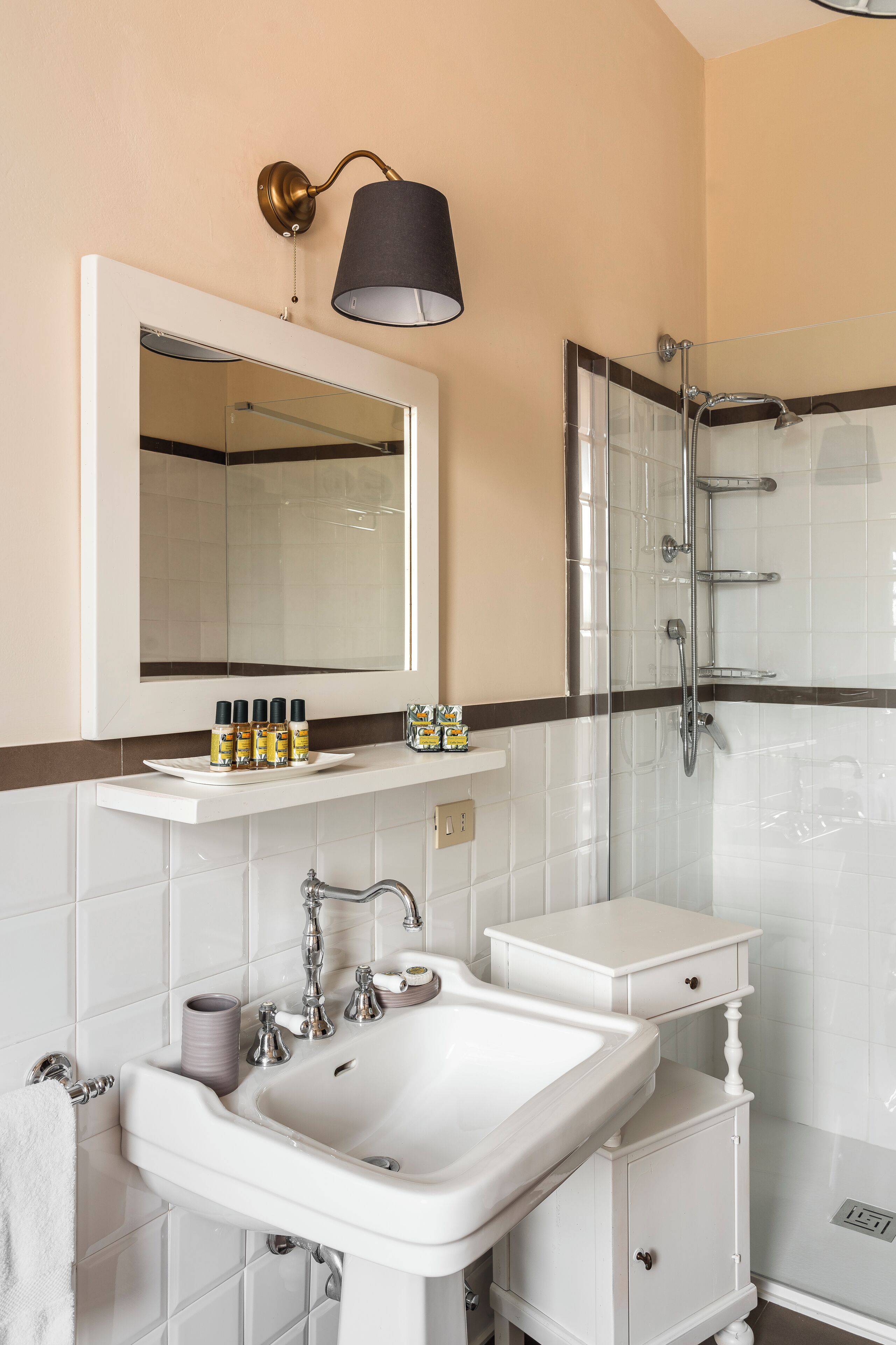 A bathroom with a white sink, mirror, and shower. There are toiletries on the sink and a towel hanging on the wall.