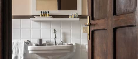 Une salle de bain avec un lavabo sur pied blanc, un miroir au-dessus et une porte en bois.