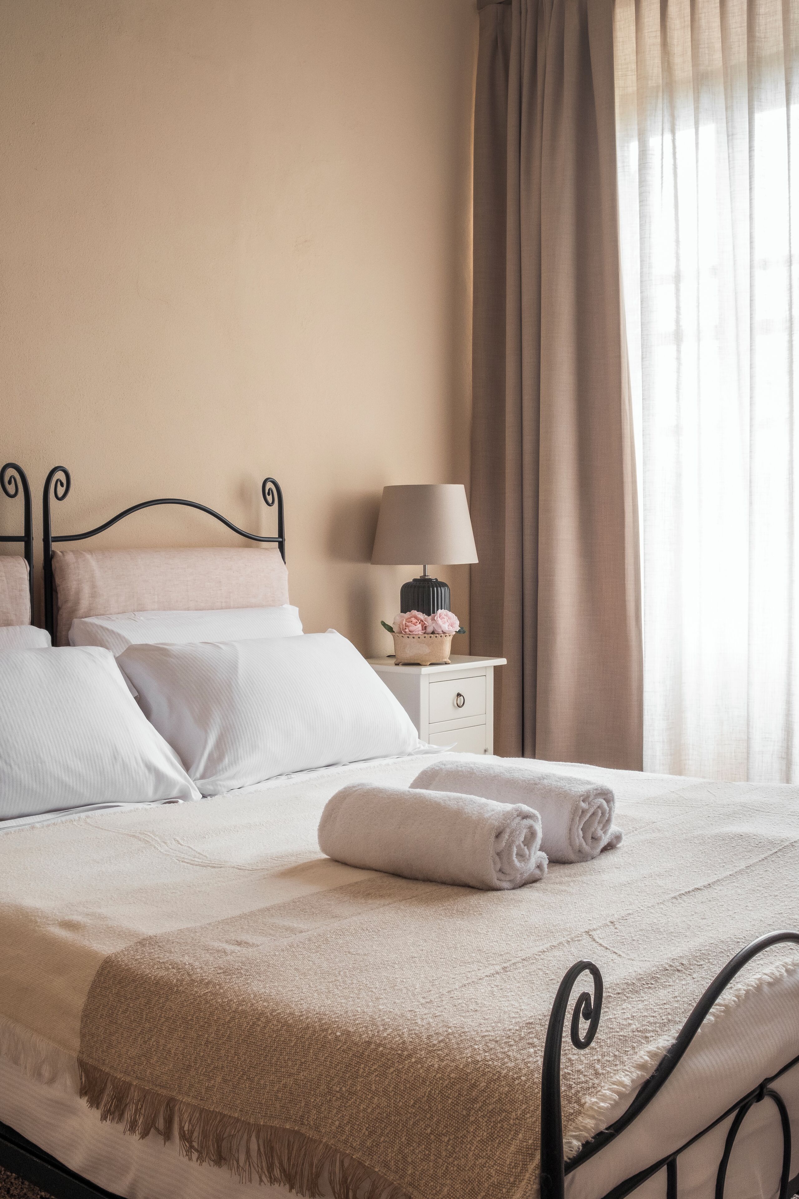 A neatly made bed with white linens, a beige throw blanket, and a lamp on a bedside table.