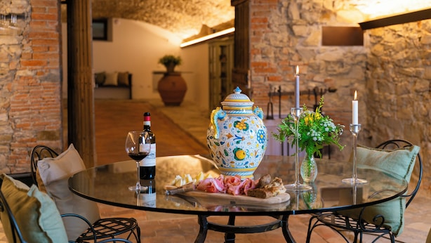 A round glass table with a bottle of wine, a vase with flowers, and a plate of food. - Villa Erbaia Relais de Charme (Barberino di Mugello)