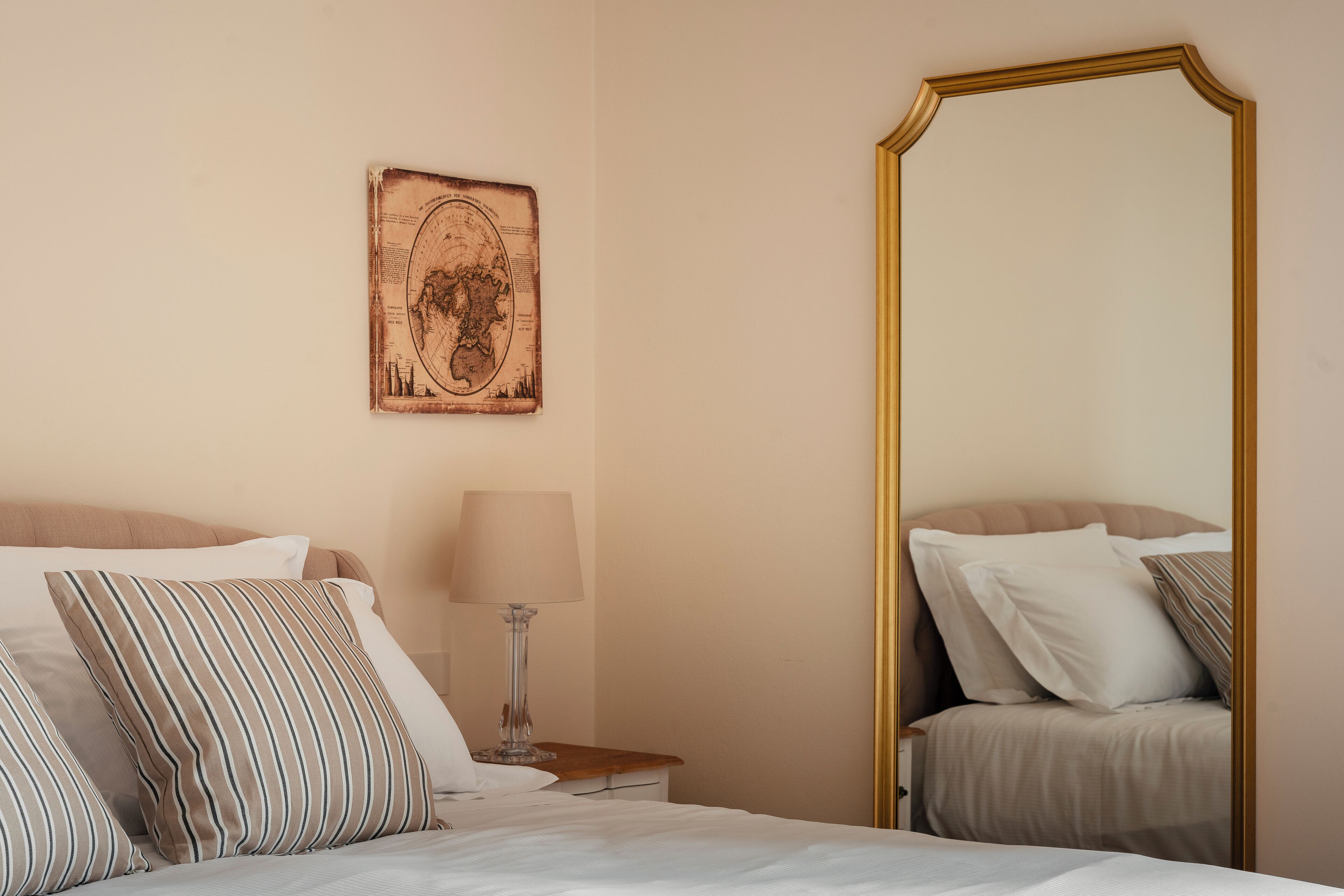A neatly made bed with striped pillows, a bedside lamp, and a large mirror with a gold frame.