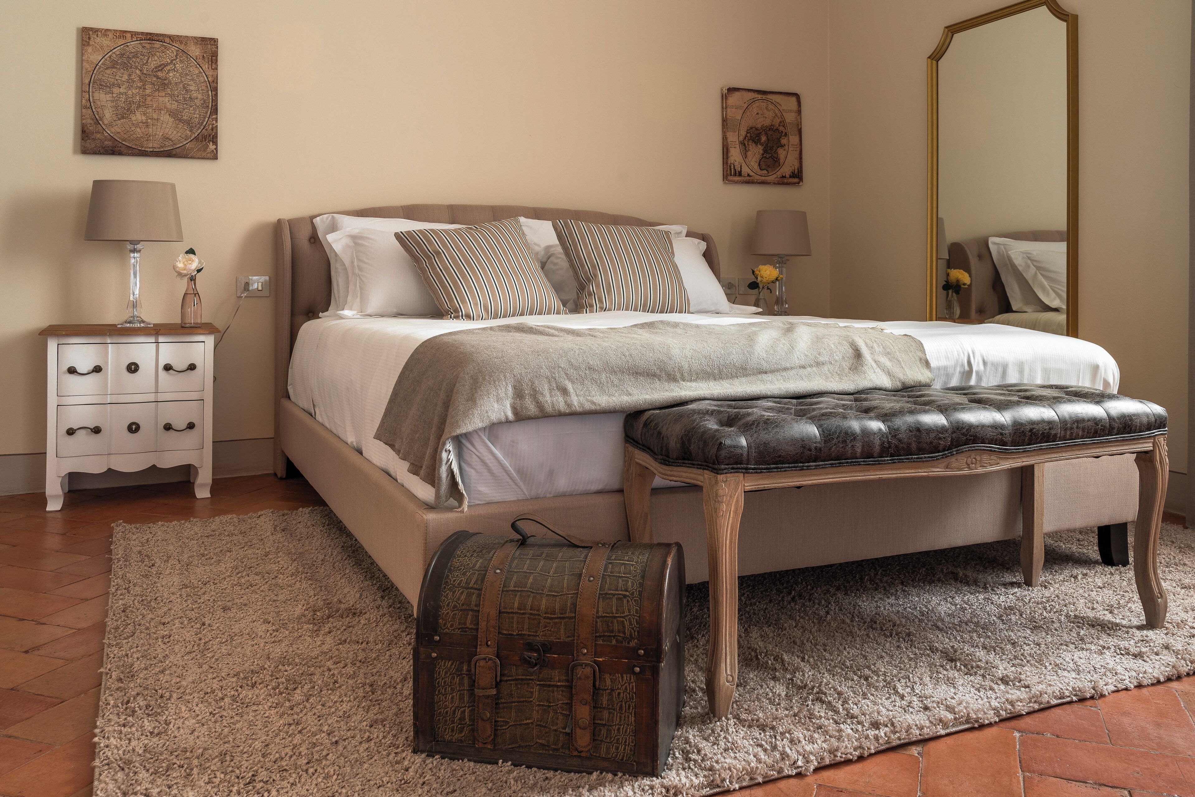 Ein Schlafzimmer mit einem Bett, Nachttischen, einem Spiegel und einem Zierkoffer.