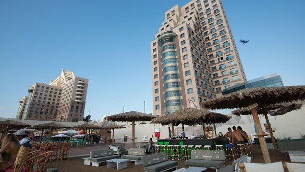 A rooftop bar with lounge chairs and umbrellas, overlooking a cityscape with tall buildings. - Beautifull apartments by the sea (Haifa)