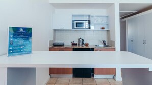 A modern kitchen with a microwave, kettle, and sink. There is a sign on the wall and a white countertop. - Beautifull apartments by the sea (Haifa)