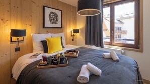 Une chambre d’hôtel moderne avec un mur en bois, un grand lit avec une literie grise, un oreiller jaune et un plateau contenant des articles pour le petit-déjeuner.