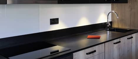 A modern kitchen with black cabinets, a black countertop, a stainless steel range hood, and a built-in oven.