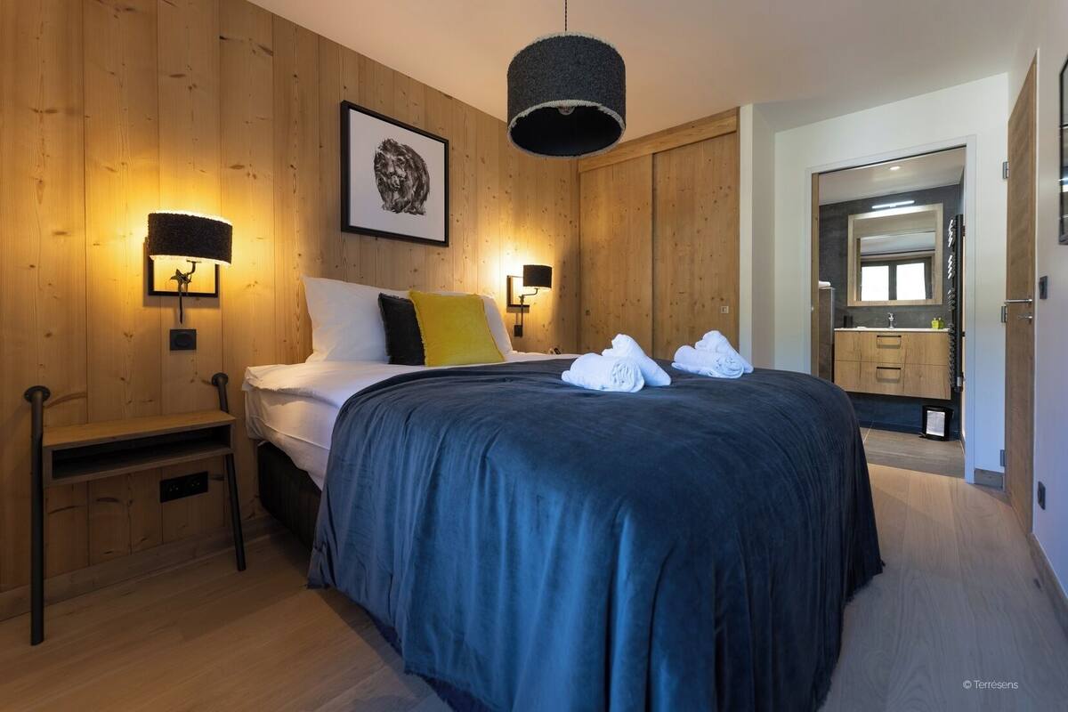 A modern bedroom with a large bed, wooden walls, and a small bedside table.