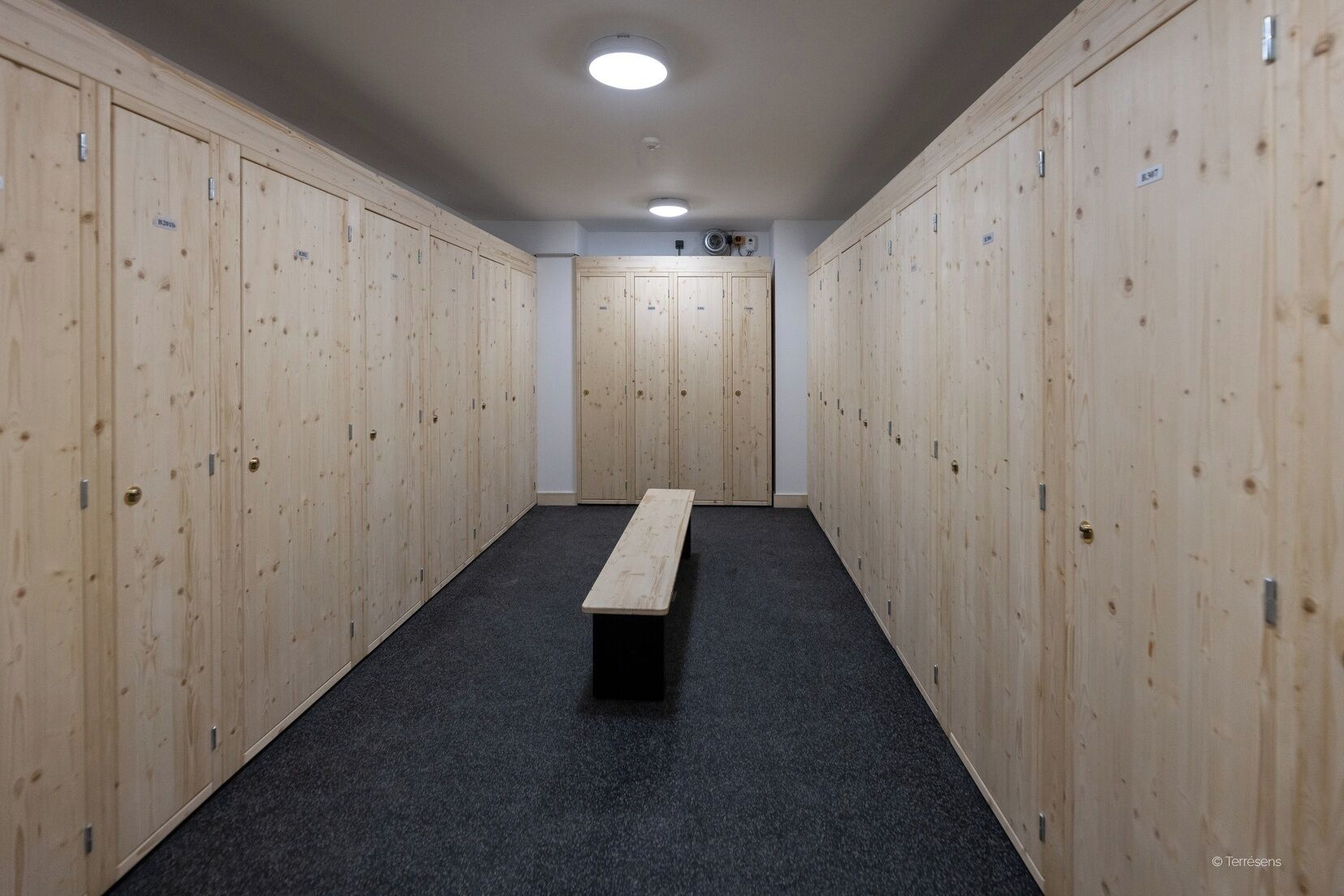 A locker room with wooden lockers, a bench, and a carpeted floor.