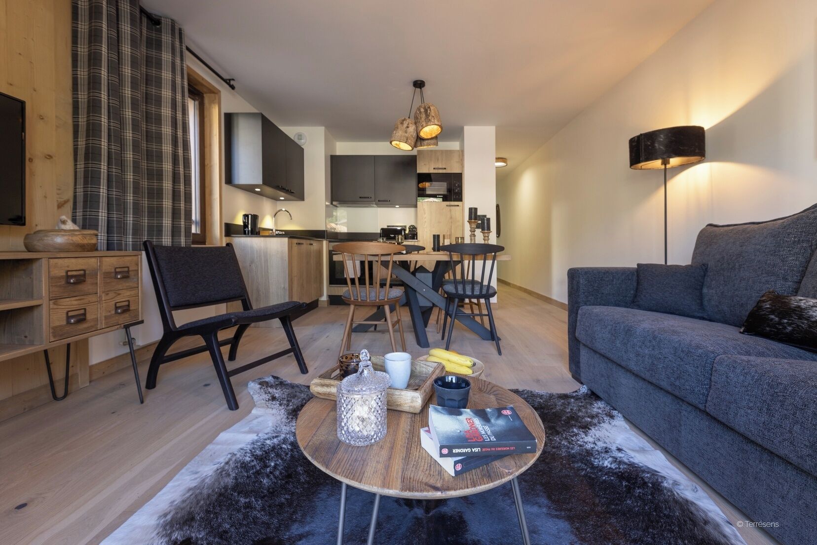 A modern living room with a grey sofa, a coffee table with books and a bowl, a black chair, and a wooden side table.