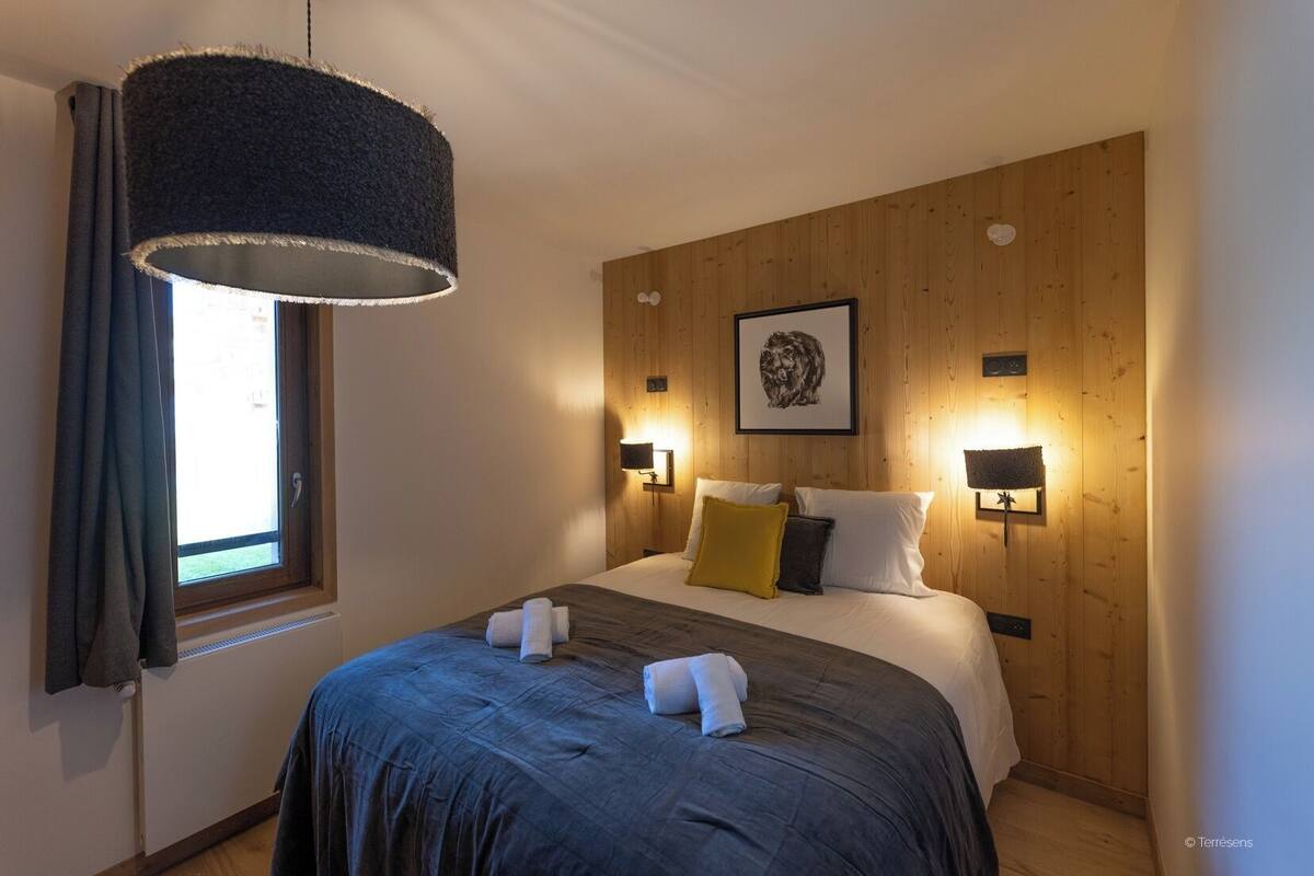 A bedroom with a large bed, two bedside lamps, a window with curtains, and a wooden headboard.